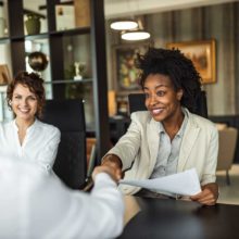 Black woman and white woman doing a business transaction, shaking hands with a while male