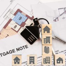 Houses and buildings on little wooden cubes with mortgage note document and keys in the background