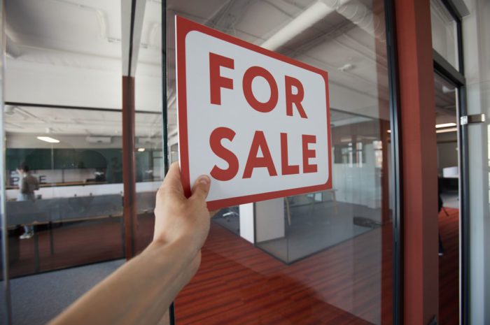 A hand putting up a for sale sign in front of glass office walls.
