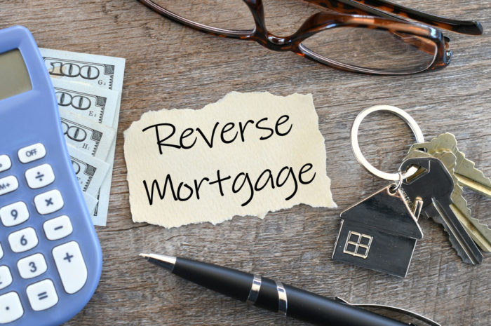 Paper with the words reverse mortgage on it along with a calculator, keys, pen, and glasses on a wooden table.